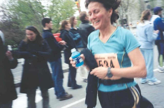 A soft-focus early-2000s race photo of Paula mid-stride, smiling, carrying a water bottle.