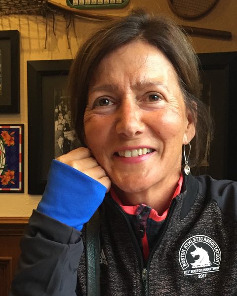 Paula Didham smiling warmly, wearing her 2017 Boston Marathon jacket.